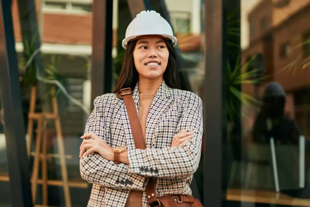 Joven arquitecta asiática con los brazos cruzados sonriendo feliz en la ciudad.